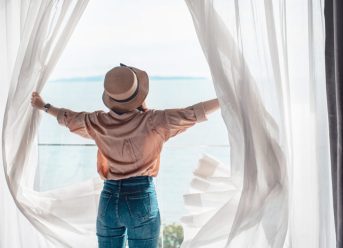 femeie care se uita la mare de pe geamul camerei de hotel